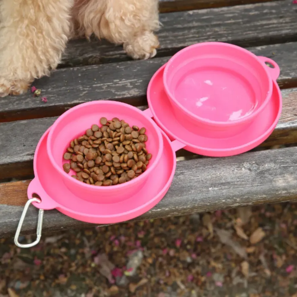 Close-up top view of an open pink silicone travel feeder with kibble in one bowl and water in the other on a wooden surface.