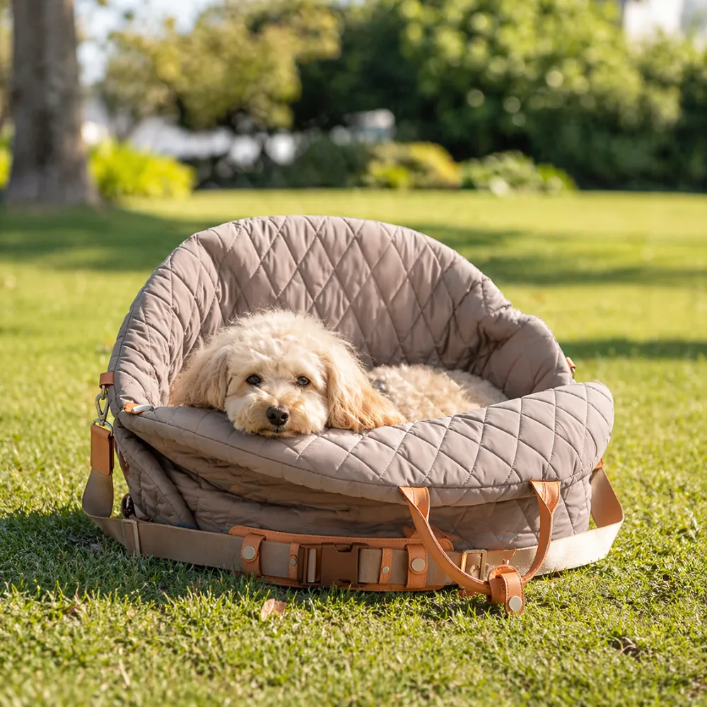 small curly dog resting inside grey quilted portable dog car bag placed on grass outdoor pet travel bed