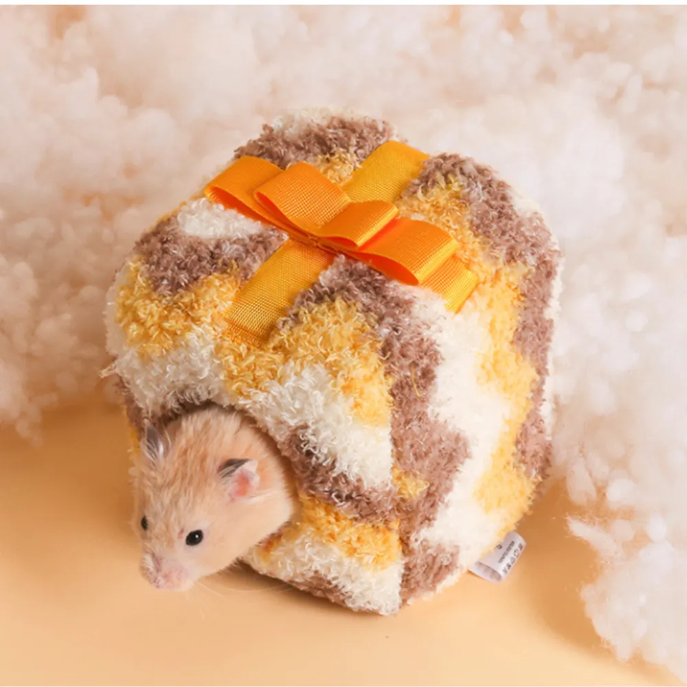 A hamster entering a yellow gift-box style plush nest on a soft white cloud-like background.