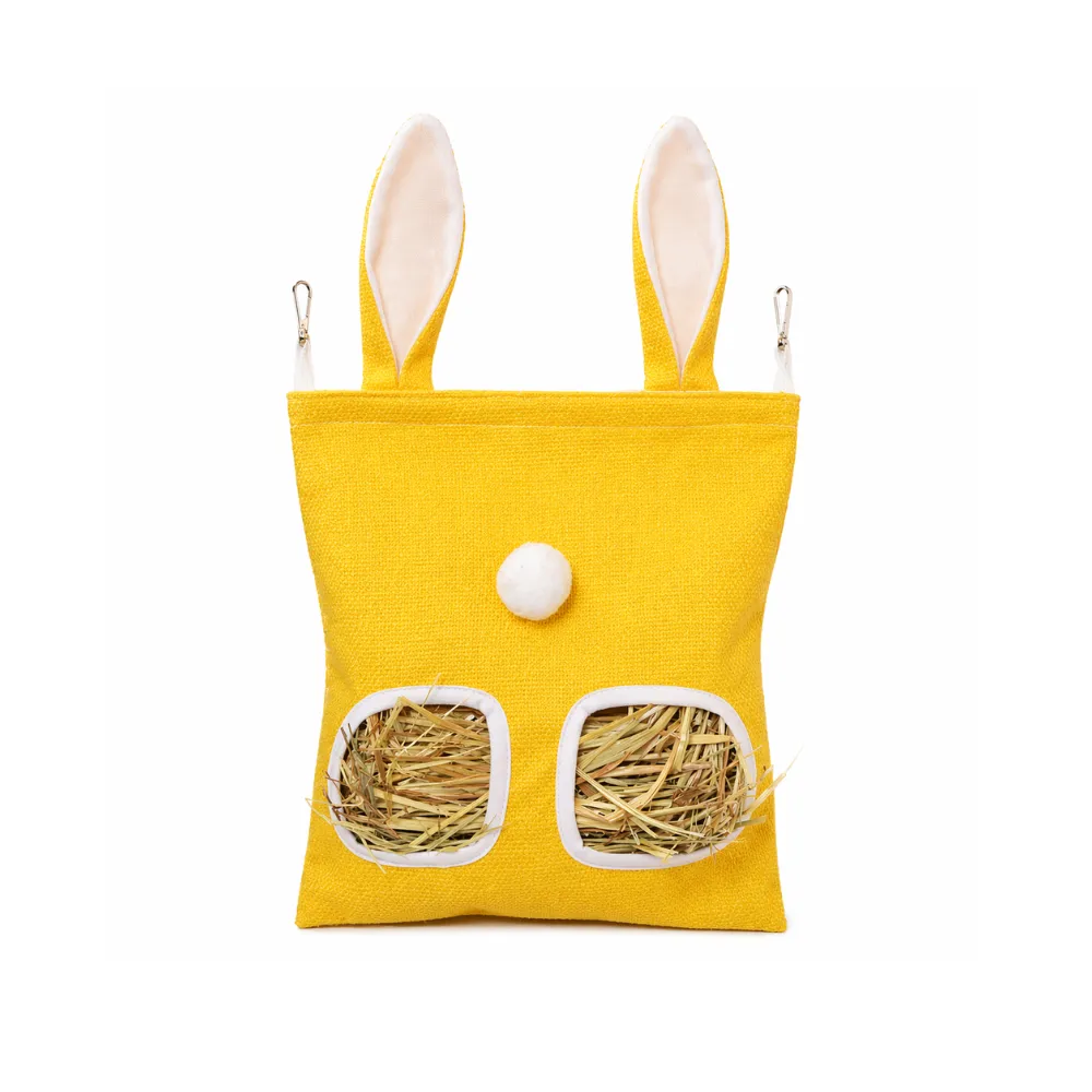 A bright yellow rabbit hay bag with two square holes filled with dried hay, featuring white ear accents.