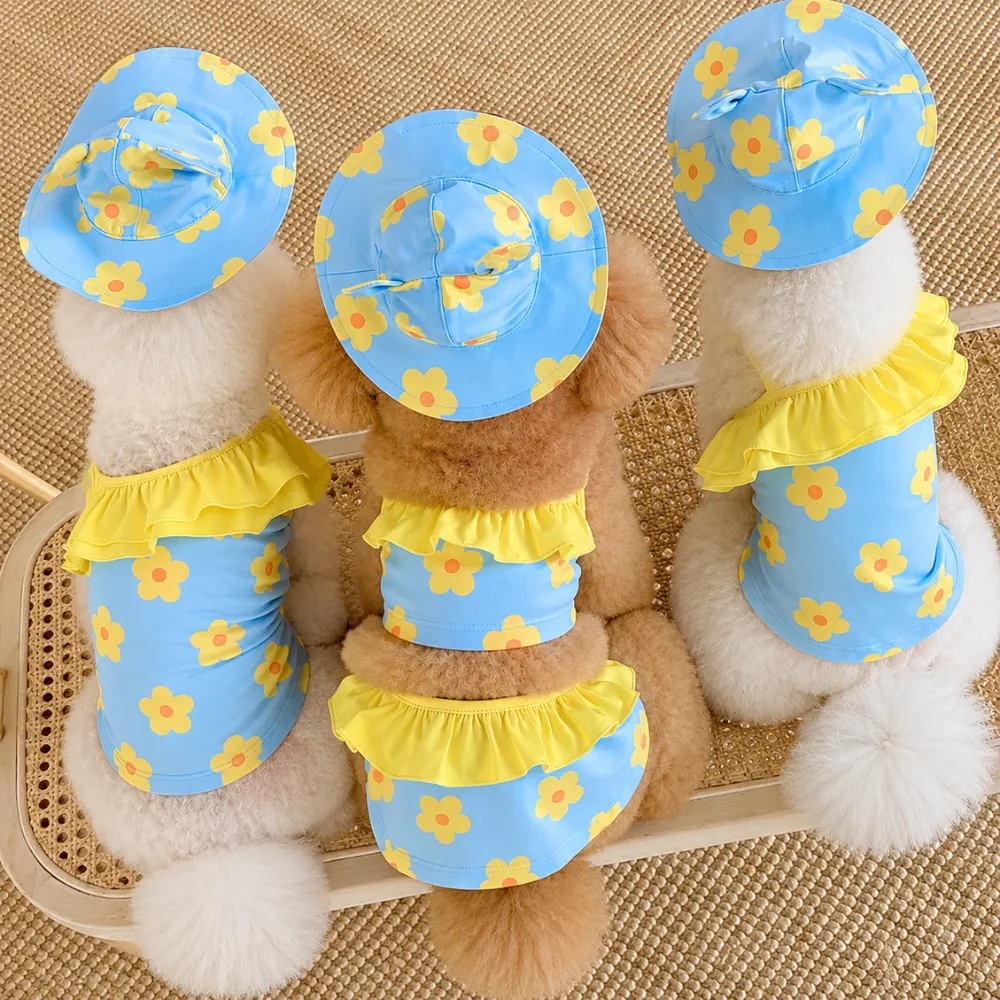 Three dogs wearing blue flower print dog swimsuits with yellow ruffles and matching hats