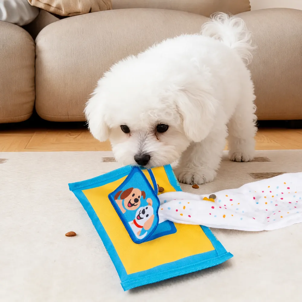 Small white puppy playing with yellow and blue tissue box dog toy during indoor enrichment and treat hunting game