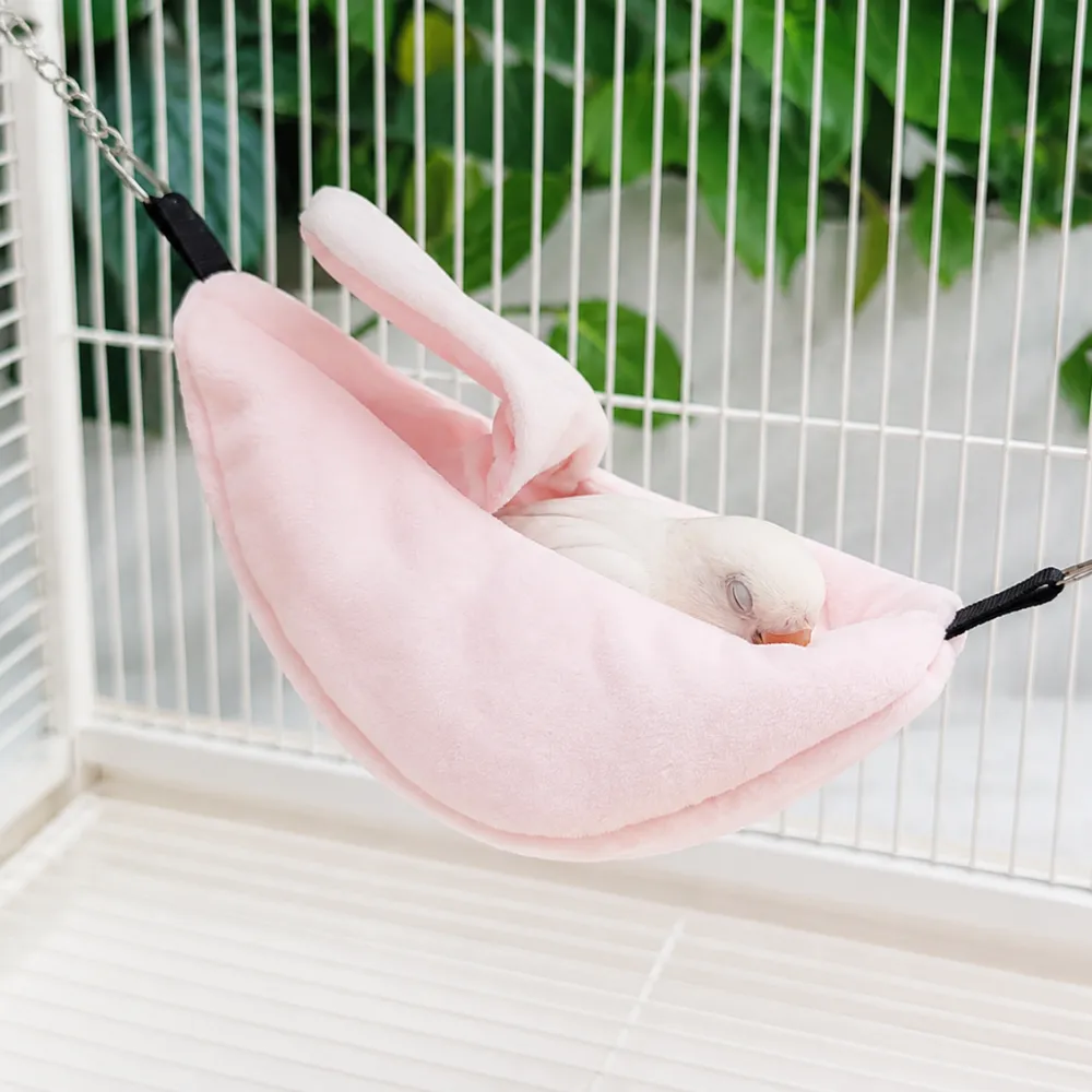 Small bird resting comfortably inside a soft banana hanging hammock nest in a bird cage