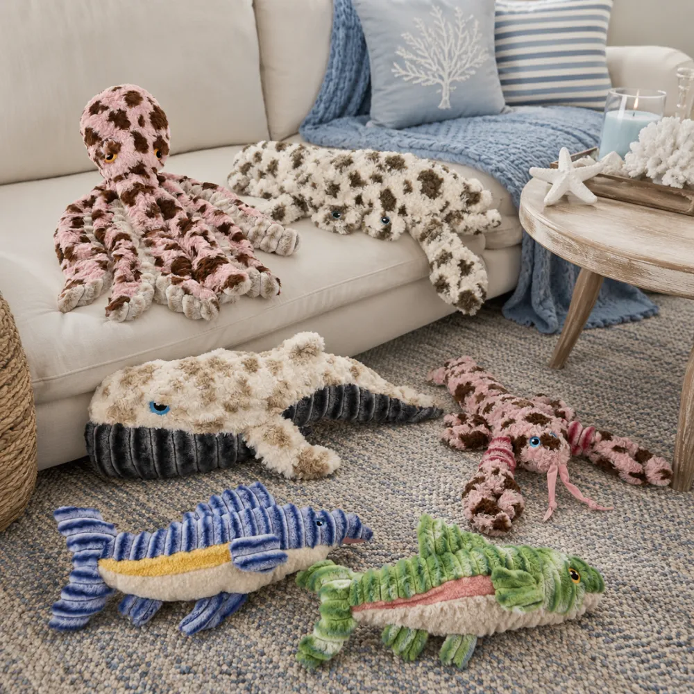 Ocean-themed plush dog toy collection displayed on a sofa, including lobster, octopus, whale, fish, crab, and alligator designs.